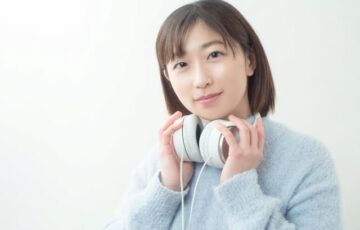 ヘッドフォンを首にかけて微笑む20代女性